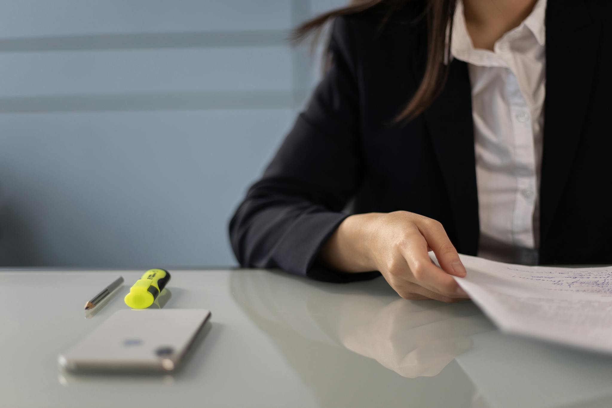 Business professional reviewing documents with highlighter and phone on glass desk, ideal for office scenes.